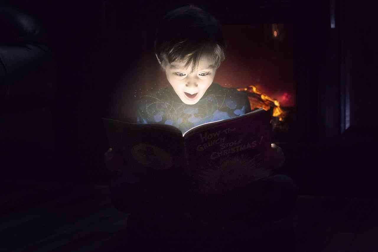 Мальчик с восторгом читает книжку под лампой